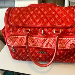 Red Vera Bradley weekender with handle and wheels. Measures 18” by 14” by 10”.